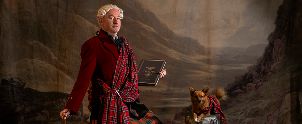 actor Martin O'Connor stands in front of a Scottish landscape, wearing a great kilt and holding the poems of Ossian, while a similarly outfitted small dog sits nearby.