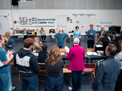 Actors have formed a huddle round a table which director Dominic Hill stands behind, giving the actors direction.