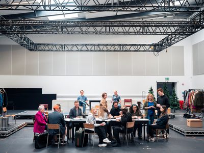 The cast of Small Acts of Love are around a table. It is an informal setting, some stand and chat and others sit.