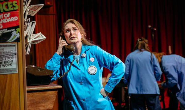 Jo Freer wears a cyan overcoat. She is speaking into a telephone and looks worried.