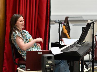 Hannah Jarret-Scott sits behind a keyboard laughing. A red curtain peeks out behind her.