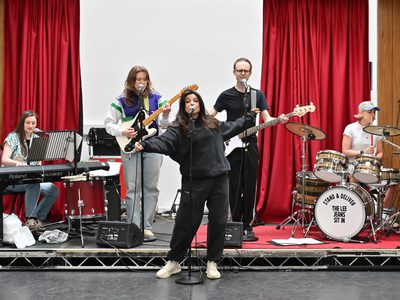 The Stand & Deliver cast stand on-stage with keyboards, guitars and drums. Chiara sings