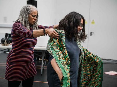 Edugie Clare Robertson looks down, placing a piece of green and yellow patterned fabric over Hannah Lavery's shoulders.