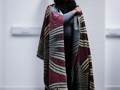 Kimberley Mandindo stands in a a rehearsal room, draped in a piece of burgundy, beige and grey patterned fabric.
