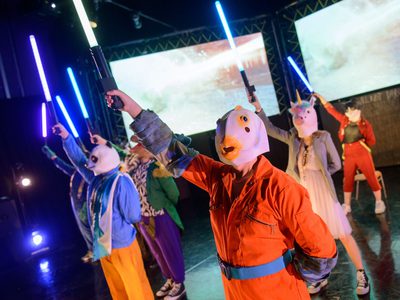 A group of young people wearing rubber animal masks hold lightsabres in the air.