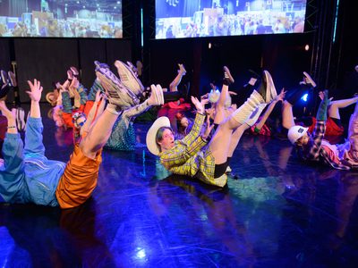 A group of young people wearing cosplay costumes lie on stage with their arms ad legs in the air.