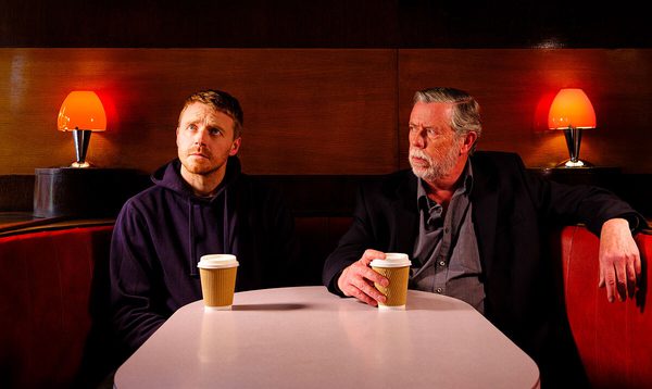 Fifth Step actors, Jack Lowden and Sean Gilder sit side-by-side in a bar booth with take away coffees