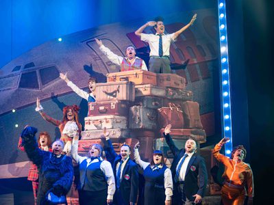 The High Life cast stand waving in front of a gigantic pile of suitcases