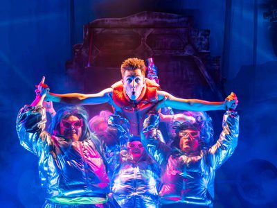 A group of people wearing neon reflective clothing hold up a man wearing the same type of outfit.