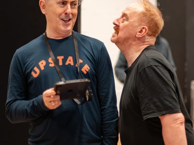 Two actors stand beside each other in a rehearsal room.