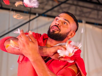 Sadiq Ali wears a red hoodie. There are feathers falling from the sky. Sadiq looks at the feathers with fascination.