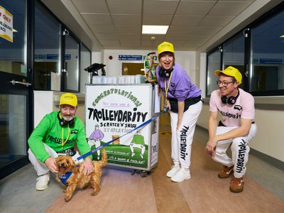 The Trolleydarity team stand with their trolley and a honey-brown lapdog. They are all smiling and the dog is happily receiving a pat.