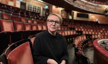 A woman is sitting in a theatre auditorium, facing towards the camera.