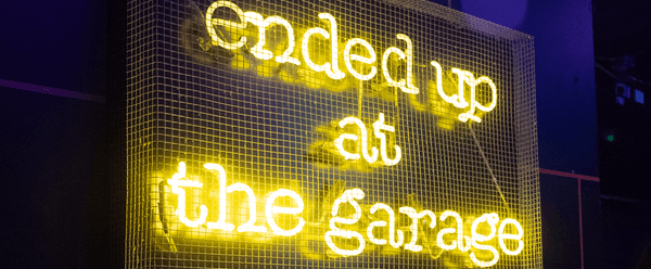 Neon yellow illuminated sign reads "ended up at the garage"