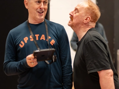 Two actors stand beside each other in a rehearsal room.
